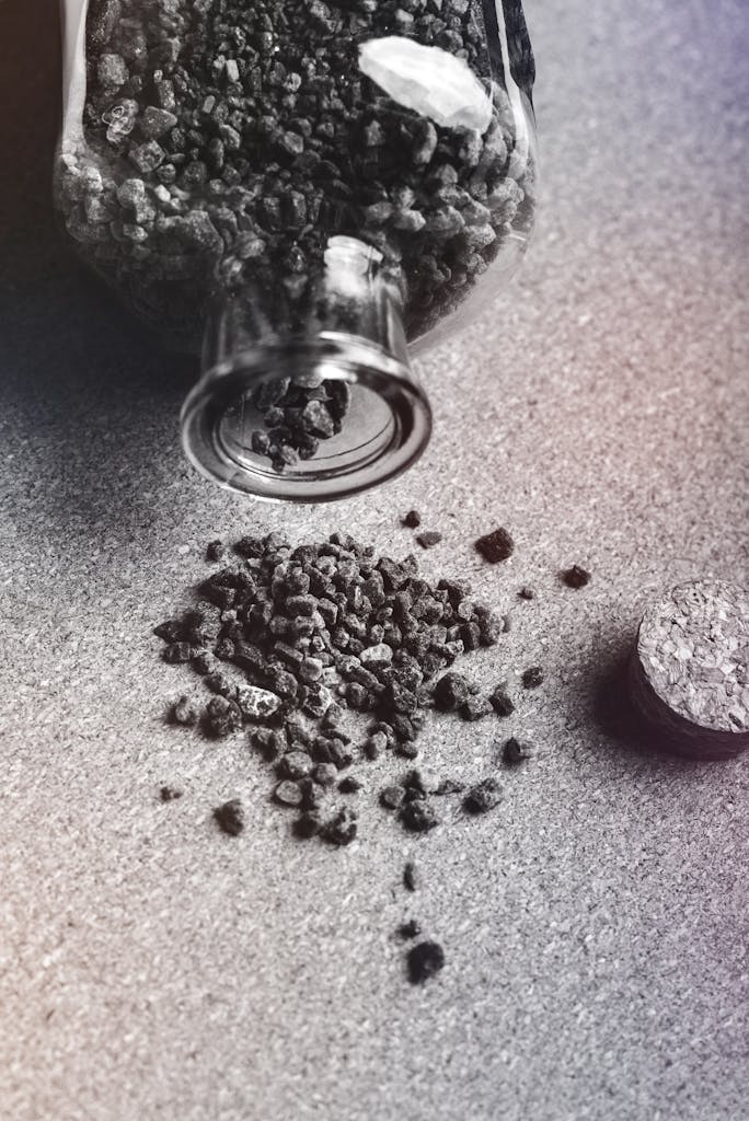 From above black and white of activated carbon granules scattered on table from glass jar with cork