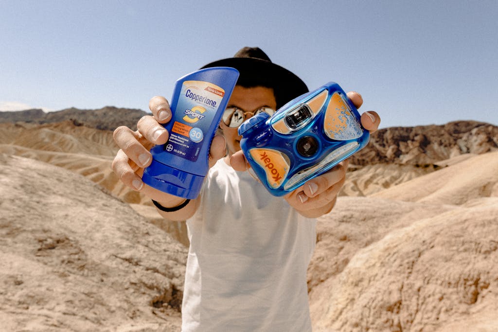 Man Holding Blue Kodak Camera and Sunscreen