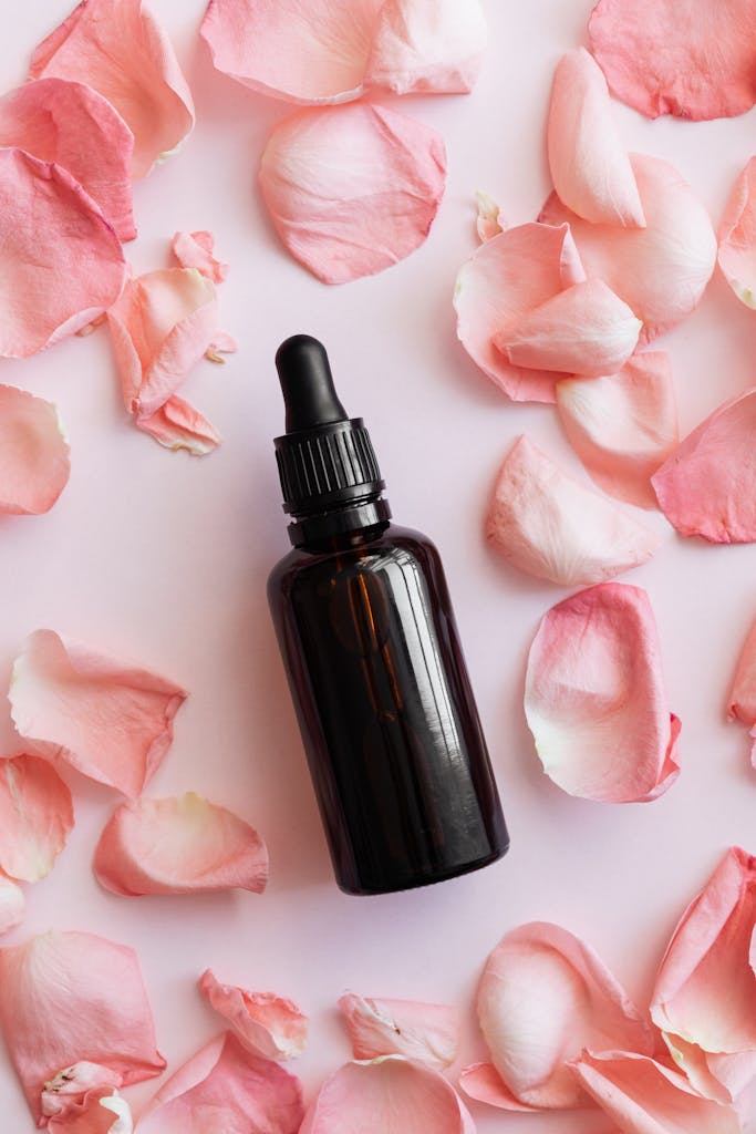 Composition of vial and pink petals on pink background