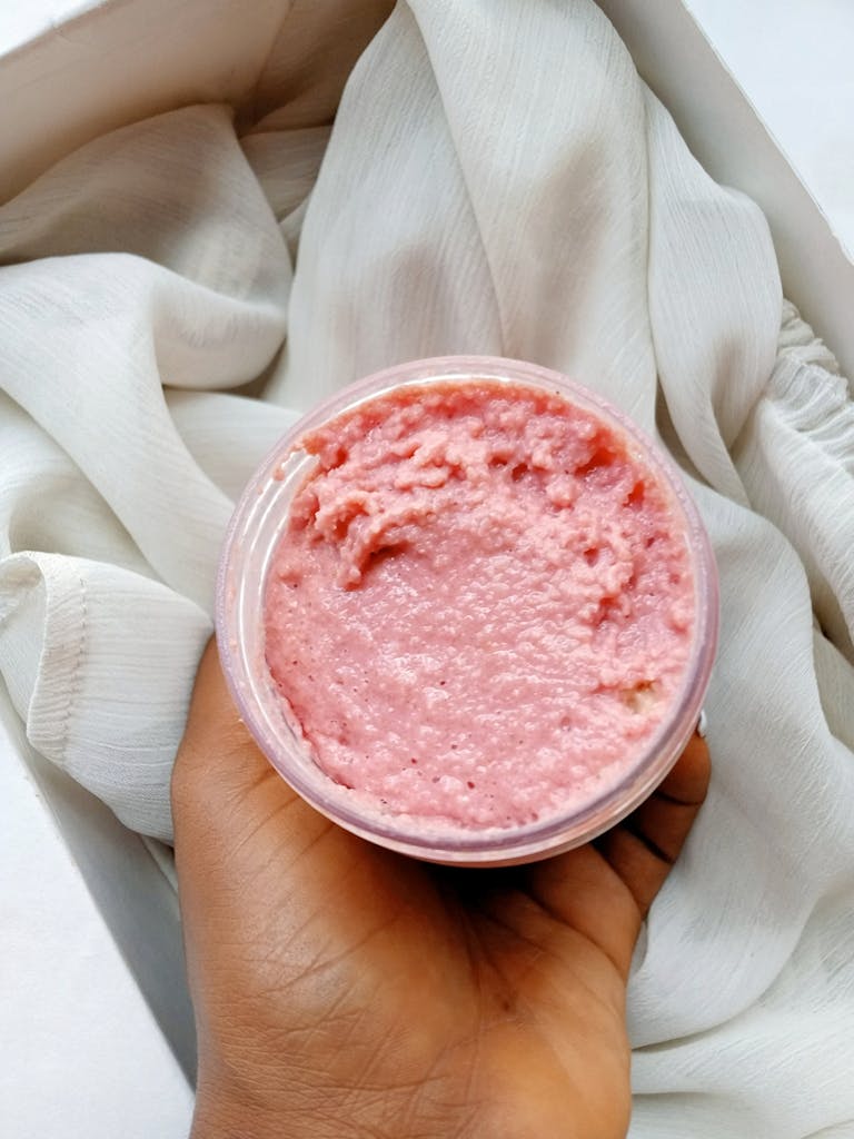 clean beauty A close-up of a hand holding a natural pink sugar body scrub jar, perfect for skincare routines.